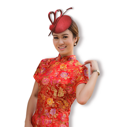 A Chinese bride in red qipao weariing a red sinamay button cocktail hat with satin ribbon in heart-shaped (decorated with 4 pieces of zicrons), a red arrow feather and red pom pom