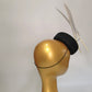 black sinamay pillbox hat with 2 floating feathers on mannequin head