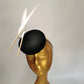 black sinamay pillbox hat with 2 floating feathers on mannequin head